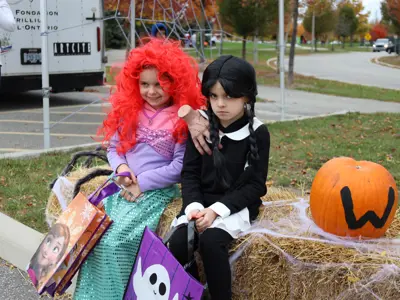 Children in costumes sitting on a bale of hay.