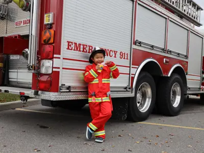 Child wearing a firefighter costume leaning against a firetruck.