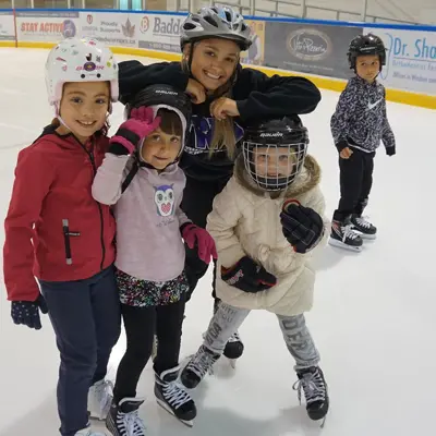 A group of children smiling and skating indoors.
