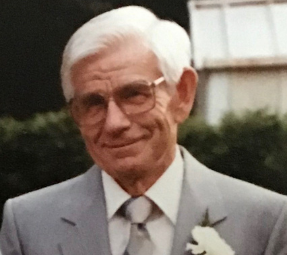 Enos Howson smiling with a grey suit and white flower