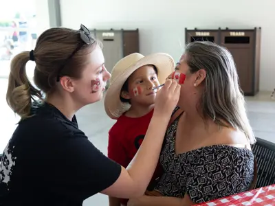 People having their faces painted with Canadian flag designs.